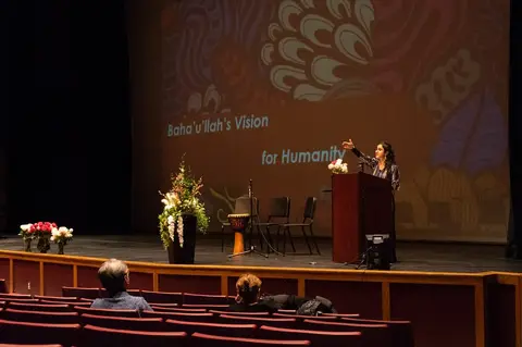A speaker on stage in an auditorium decorated with flowers