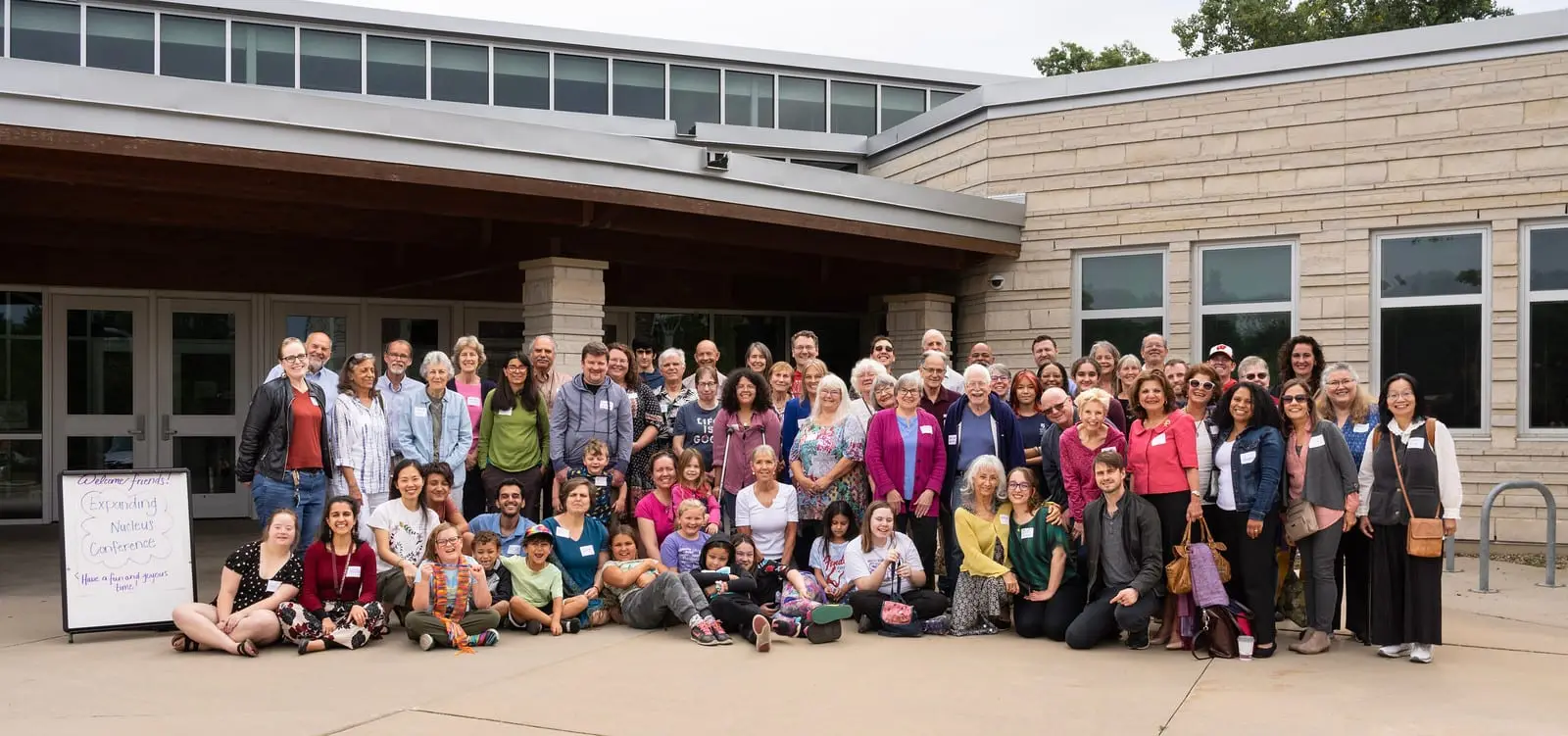 A large group of friends of all ages gathered outdoors in front of a meeting hall